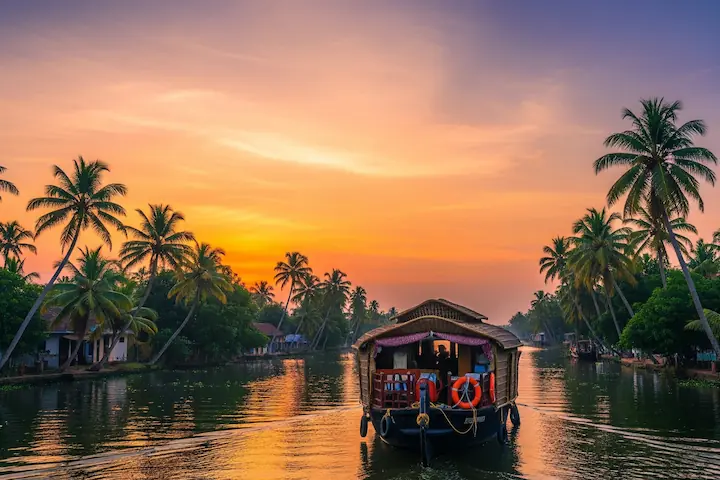 Kerala backwater tour packages showcasing a traditional houseboat cruising through palm-lined canals at sunset in Kerala backwaters